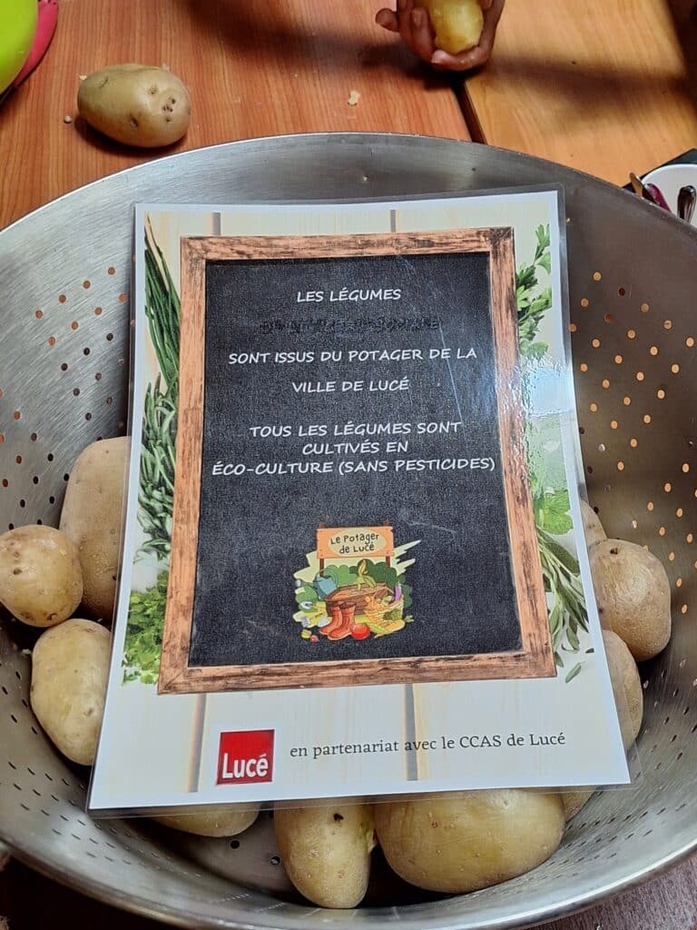 Panier de pommes de terre sur une table, avec une affiche indiquant qu’elles proviennent du potager de la ville de Lucé et sont cultivées en éco-culture.